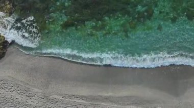 Drone gri gökyüzünün altında taşlarla mavi sahili yakalıyor..