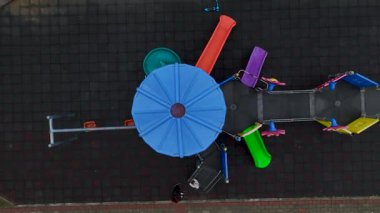 Çocuklar renkli slayt setinin yanında salıncakların keyfini çıkarıyorlar.