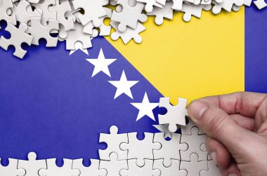Bosna-Hersek bayrağı üzerinde insan el kıvrımlar bir bulmaca beyaz renk bir tablo üzerinde tasvir.