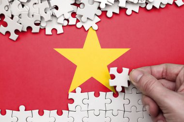 Vietnam flag  is depicted on a table on which the human hand folds a puzzle of white color. clipart