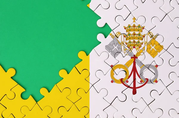 Vatican City State flag  is depicted on a completed jigsaw puzzle with free green copy space on the left side.