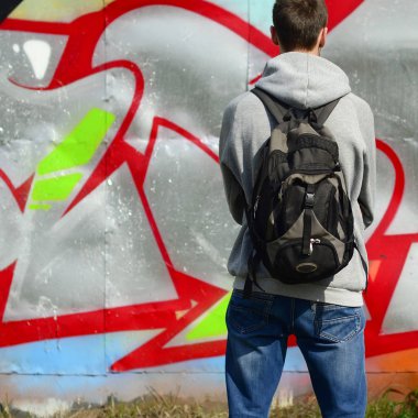 Siyah bir çanta ile bir genç grafiti sanatçısı duvara onun grafiti ile bir duvar üzerinde görünüyor. Sokak sanatı kavramı.