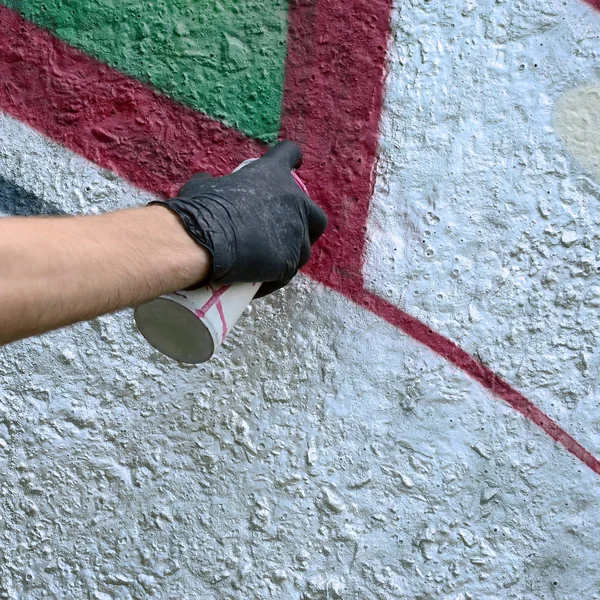 A hand in black gloves paints graffiti on a concrete wall. Illegal vandalism concept. Street art.