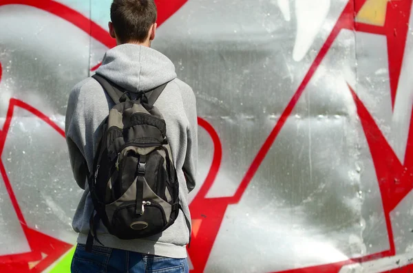 A young graffiti artist with a black bag looks at the wall with his graffiti on a wall. Street art concept.
