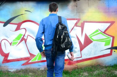 Siyah bir çanta ile bir genç grafiti sanatçısı duvara onun grafiti ile bir duvar üzerinde görünüyor. Sokak sanatı kavramı.