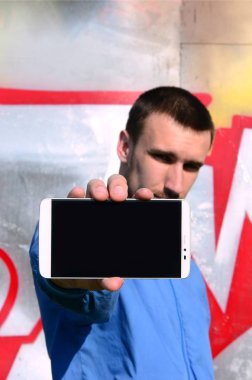 Grafiti sanatçısı bir smartphone ile renkli boyalı duvar arka planı boş bir siyah ekran gösterir. Sokak sanatı kavramı.