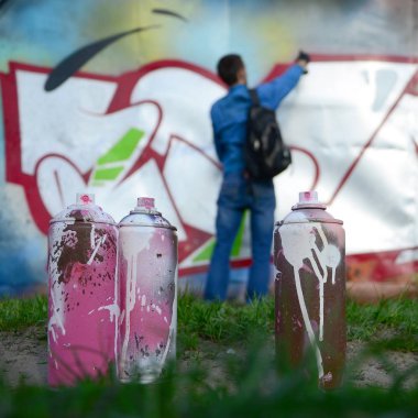 Birkaç kullanılan boya kutuları üzerinde büyük grafiti çizim genç adam çizer duvar boşlukla arka planı. Duvar grafiti çizim Modern Sanat.