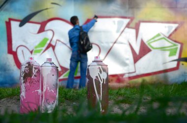 Birkaç kullanılan boya kutuları üzerinde büyük grafiti çizim genç adam çizer duvar boşlukla arka planı. Duvar grafiti çizim Modern Sanat.