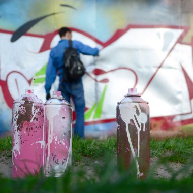 Birkaç kullanılan boya kutuları üzerinde büyük grafiti çizim genç adam çizer duvar boşlukla arka planı. Duvar grafiti çizim Modern Sanat.