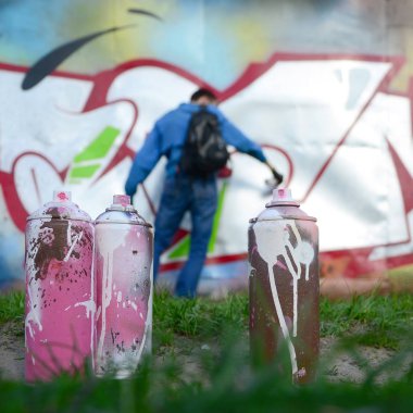 Birkaç kullanılan boya kutuları üzerinde büyük grafiti çizim genç adam çizer duvar boşlukla arka planı. Duvar grafiti çizim Modern Sanat.