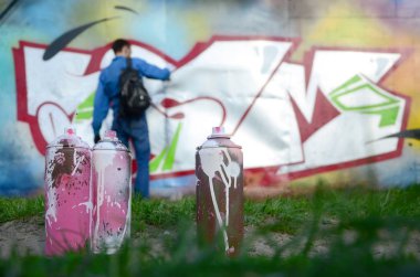 Birkaç kullanılan boya kutuları üzerinde büyük grafiti çizim genç adam çizer duvar boşlukla arka planı. Duvar grafiti çizim Modern Sanat.