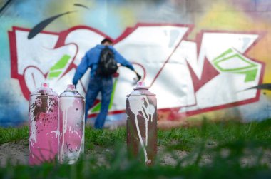 Birkaç kullanılan boya kutuları üzerinde büyük grafiti çizim genç adam çizer duvar boşlukla arka planı. Duvar grafiti çizim Modern Sanat.