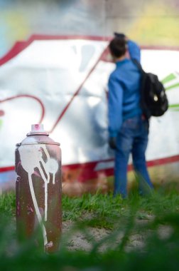 Birkaç kullanılan boya kutuları üzerinde büyük grafiti çizim genç adam çizer duvar boşlukla arka planı. Duvar grafiti çizim Modern Sanat.