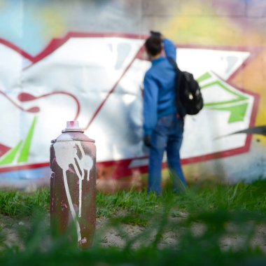 Birkaç kullanılan boya kutuları üzerinde büyük grafiti çizim genç adam çizer duvar boşlukla arka planı. Duvar grafiti çizim Modern Sanat.