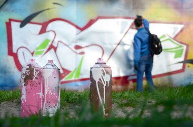 Birkaç kullanılan boya kutuları üzerinde büyük grafiti çizim genç adam çizer duvar boşlukla arka planı. Duvar grafiti çizim Modern Sanat.