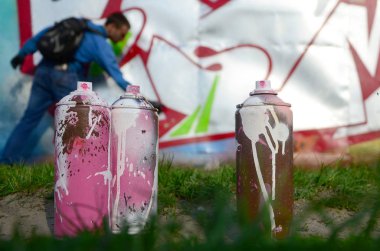 Birkaç kullanılan boya kutuları üzerinde büyük grafiti çizim genç adam çizer duvar boşlukla arka planı. Duvar grafiti çizim Modern Sanat.