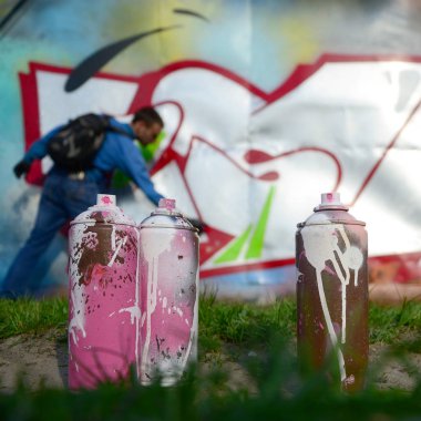 Birkaç kullanılan boya kutuları üzerinde büyük grafiti çizim genç adam çizer duvar boşlukla arka planı. Duvar grafiti çizim Modern Sanat.