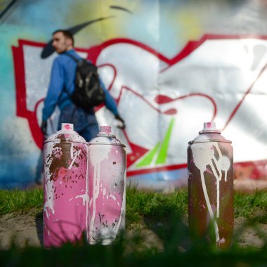 Birkaç kullanılan boya kutuları üzerinde büyük grafiti çizim genç adam çizer duvar boşlukla arka planı. Duvar grafiti çizim Modern Sanat.