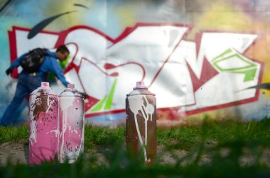 Birkaç kullanılan boya kutuları üzerinde büyük grafiti çizim genç adam çizer duvar boşlukla arka planı. Duvar grafiti çizim Modern Sanat.