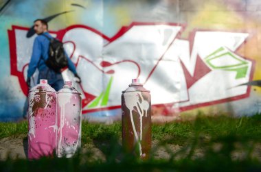Birkaç kullanılan boya kutuları üzerinde büyük grafiti çizim genç adam çizer duvar boşlukla arka planı. Duvar grafiti çizim Modern Sanat.