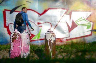 Birkaç kullanılan boya kutuları üzerinde büyük grafiti çizim genç adam çizer duvar boşlukla arka planı. Duvar grafiti çizim Modern Sanat.