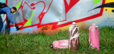 Birkaç kullanılan boya kutuları üzerinde büyük grafiti çizim genç adam çizer duvar boşlukla arka planı. Duvar grafiti çizim Modern Sanat.