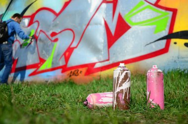Birkaç kullanılan boya kutuları üzerinde büyük grafiti çizim genç adam çizer duvar boşlukla arka planı. Duvar grafiti çizim Modern Sanat.
