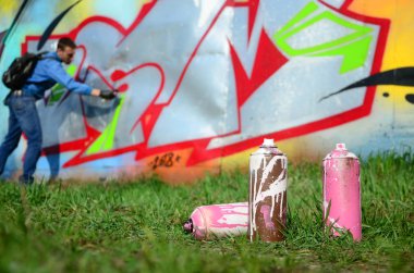 Birkaç kullanılan boya kutuları üzerinde büyük grafiti çizim genç adam çizer duvar boşlukla arka planı. Duvar grafiti çizim Modern Sanat.
