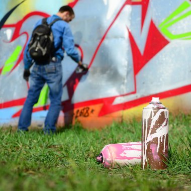 Birkaç kullanılan boya kutuları üzerinde büyük grafiti çizim genç adam çizer duvar boşlukla arka planı. Duvar grafiti çizim Modern Sanat.