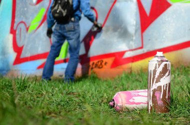 Birkaç kullanılan boya kutuları üzerinde büyük grafiti çizim genç adam çizer duvar boşlukla arka planı. Duvar grafiti çizim Modern Sanat.