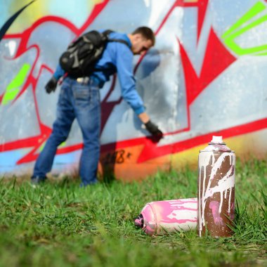 Birkaç kullanılan boya kutuları üzerinde büyük grafiti çizim genç adam çizer duvar boşlukla arka planı. Duvar grafiti çizim Modern Sanat.