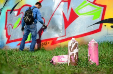 Birkaç kullanılan boya kutuları üzerinde büyük grafiti çizim genç adam çizer duvar boşlukla arka planı. Duvar grafiti çizim Modern Sanat.