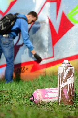 Birkaç kullanılan boya kutuları üzerinde büyük grafiti çizim genç adam çizer duvar boşlukla arka planı. Duvar grafiti çizim Modern Sanat.