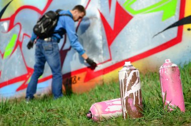 Birkaç kullanılan boya kutuları üzerinde büyük grafiti çizim genç adam çizer duvar boşlukla arka planı. Duvar grafiti çizim Modern Sanat.