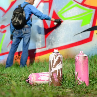 Birkaç kullanılan boya kutuları üzerinde büyük grafiti çizim genç adam çizer duvar boşlukla arka planı. Duvar grafiti çizim Modern Sanat.