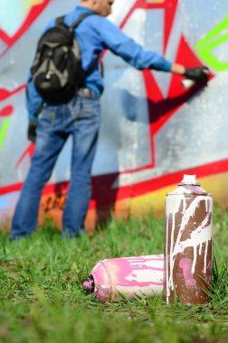 Birkaç kullanılan boya kutuları üzerinde büyük grafiti çizim genç adam çizer duvar boşlukla arka planı. Duvar grafiti çizim Modern Sanat.