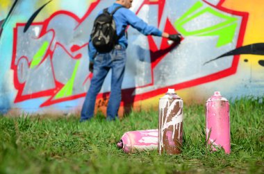 Birkaç kullanılan boya kutuları üzerinde büyük grafiti çizim genç adam çizer duvar boşlukla arka planı. Duvar grafiti çizim Modern Sanat.