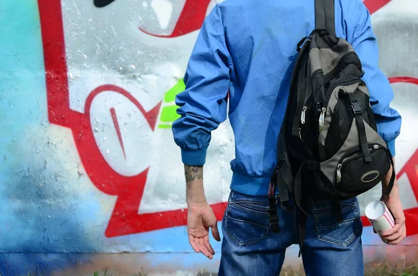 A young graffiti artist with a black bag looks at the wall with his graffiti on a wall. Street art concept.