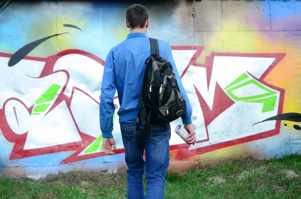 A young graffiti artist with a black bag looks at the wall with his graffiti on a wall. Street art concept.