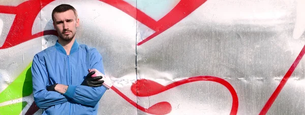 The graffiti artist with spray can poses against the background of a colorful painted wall. Street art concept.