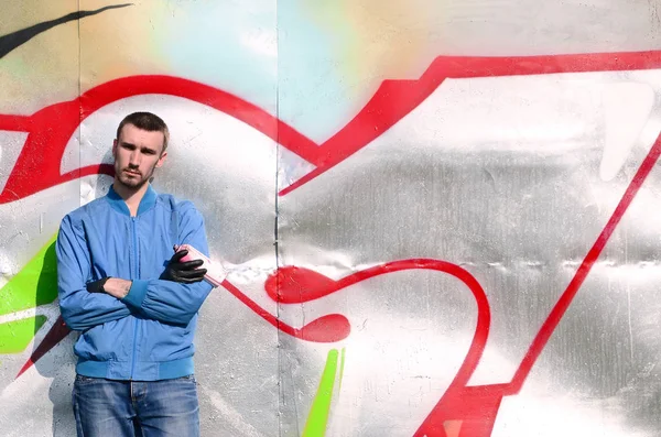 The graffiti artist with spray can poses against the background of a colorful painted wall. Street art concept.