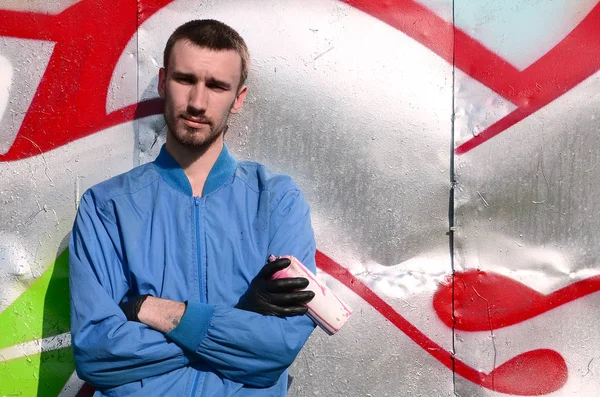 The graffiti artist with spray can poses against the background of a colorful painted wall. Street art concept.