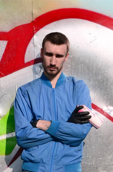 The graffiti artist with spray can poses against the background of a colorful painted wall. Street art concept.