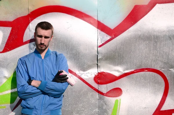 The graffiti artist with spray can poses against the background of a colorful painted wall. Street art concept.