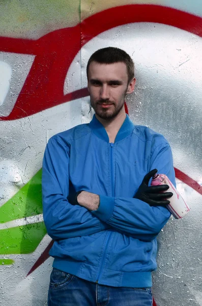 The graffiti artist with spray can poses against the background of a colorful painted wall. Street art concept.