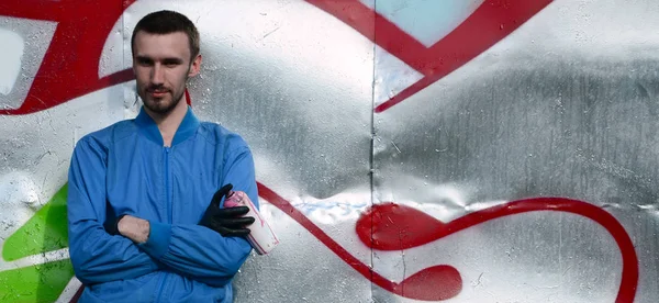 The graffiti artist with spray can poses against the background of a colorful painted wall. Street art concept.