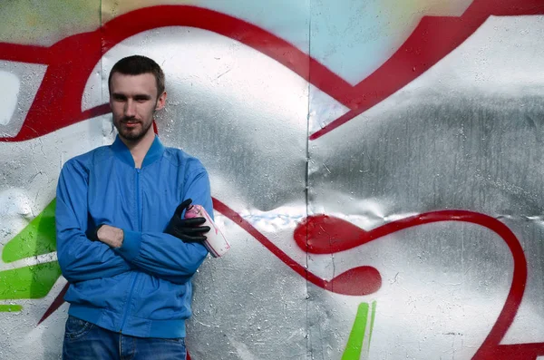 The graffiti artist with spray can poses against the background of a colorful painted wall. Street art concept.