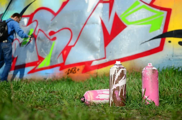 Birkaç kullanılan boya kutuları üzerinde büyük grafiti çizim genç adam çizer duvar boşlukla arka planı. Duvar grafiti çizim Modern Sanat.