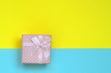 Küçük pembe hediye kutusu yalan doku arka planda moda pastel mavi ve sarı renkler kağıt en az kavramında.