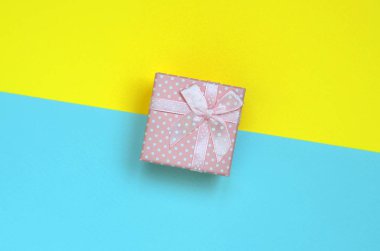 Küçük pembe hediye kutusu yalan doku arka planda moda pastel mavi ve sarı renkler kağıt en az kavramında.